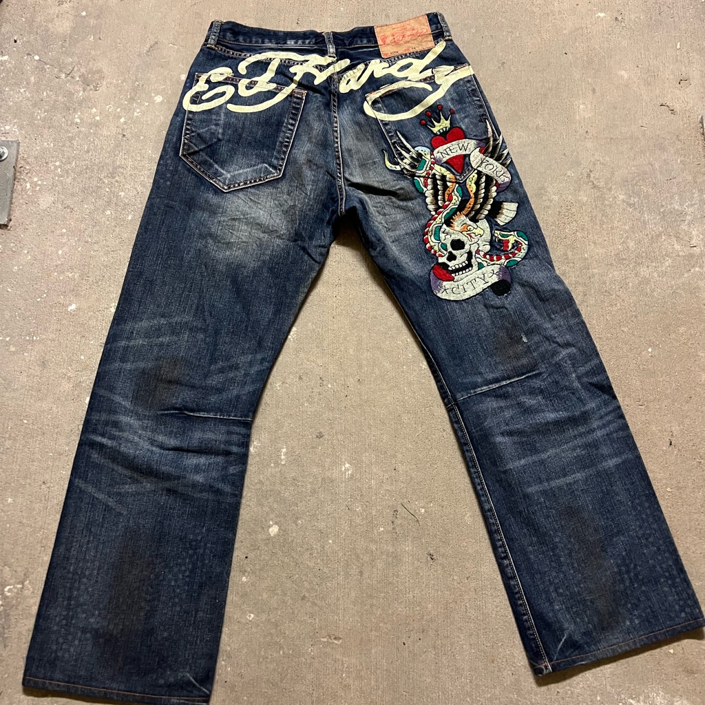 Ed Hardy dark wash bootcut jeans laid flat, with a large embroidered tiger and script back-pocket artwork covering the leg